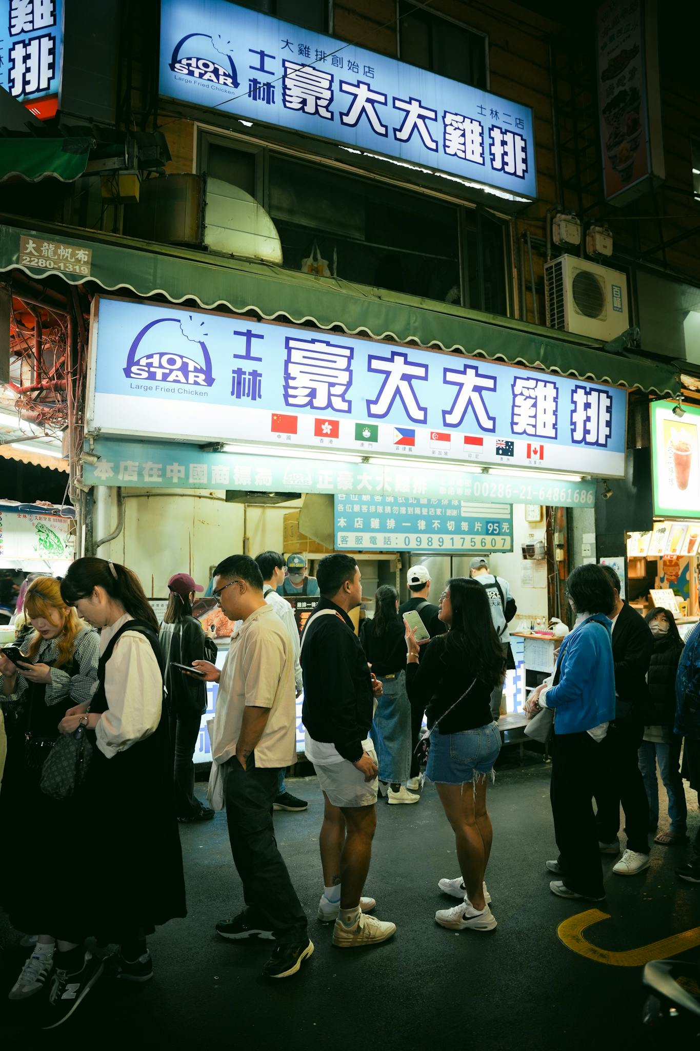 People queueing at a street food stall in a lively night market, showcasing vibrant local culture.