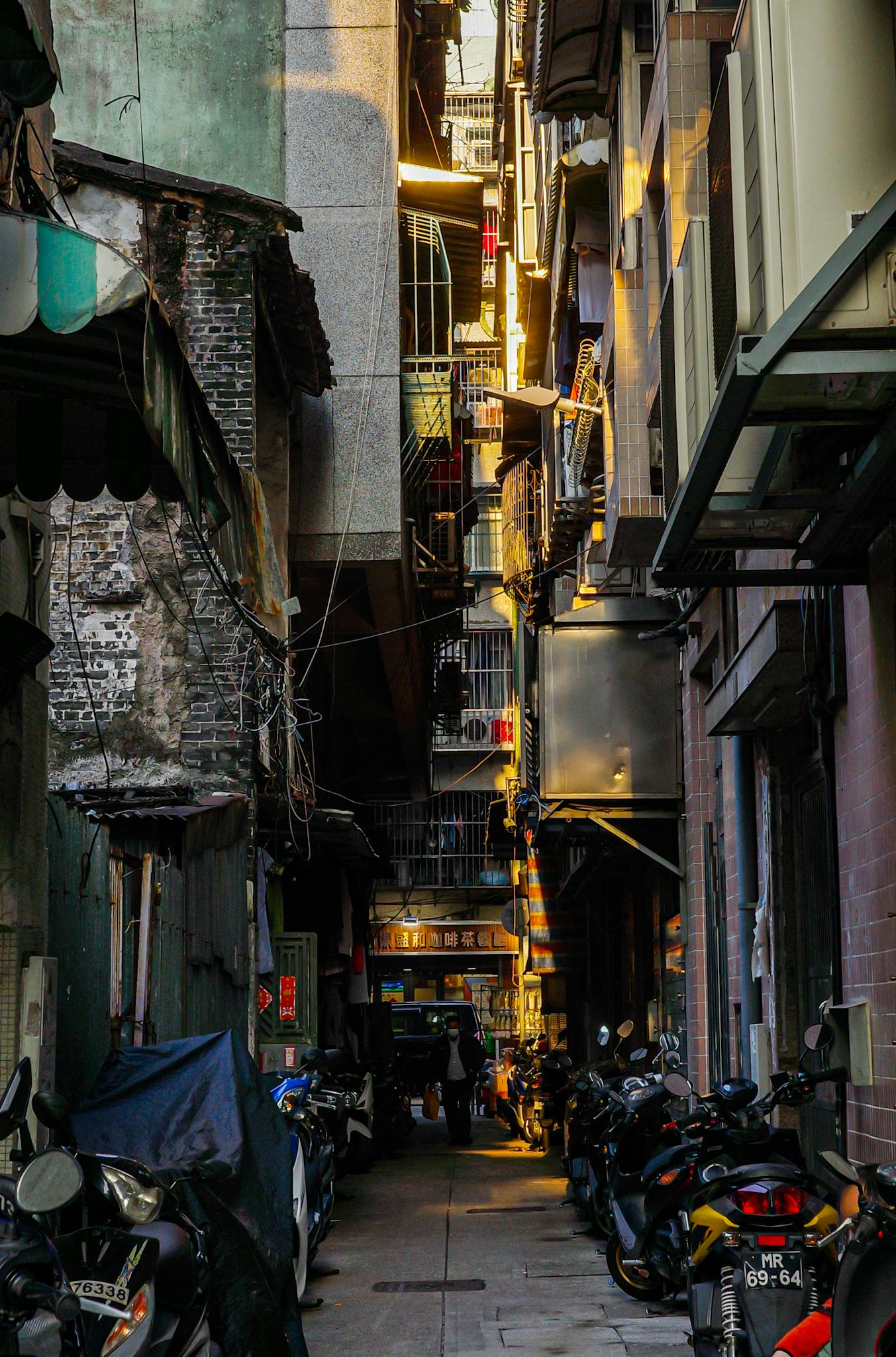Sunlight filters through a narrow Macau alley lined with motorbikes, showcasing urban street life.
