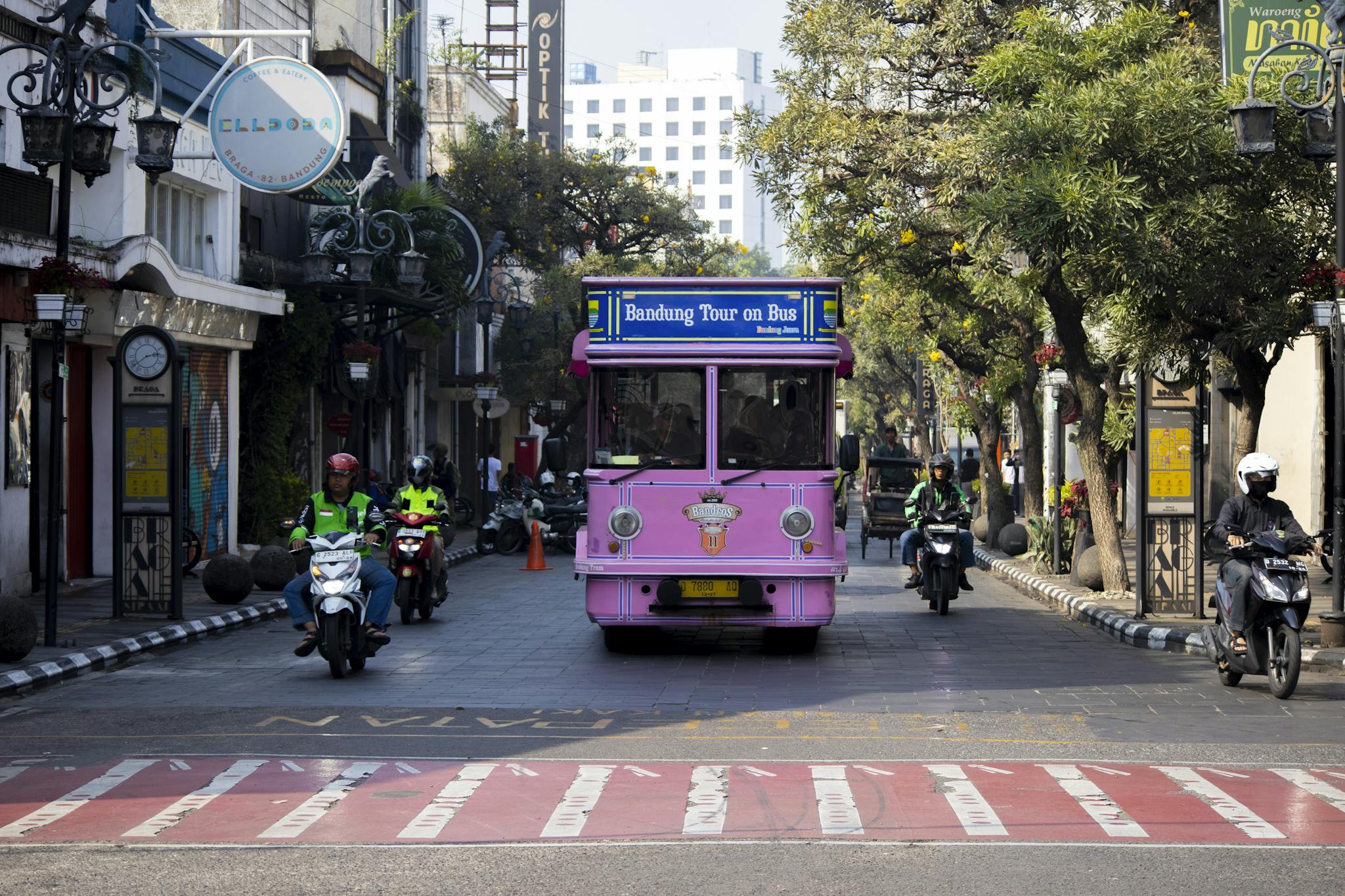 Vibrant pink tour bus and motorcyclists on a busy street in Bandung, Indonesia.